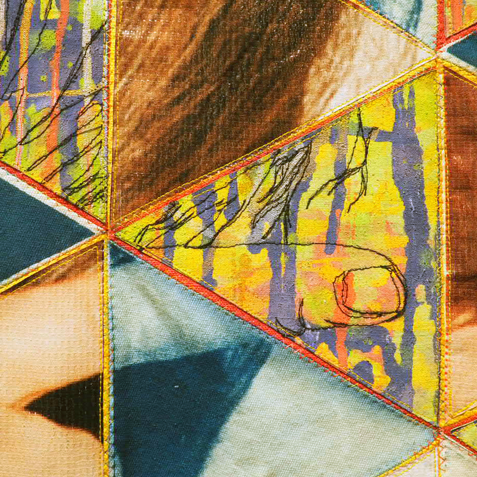 Close-up of a textile art piece with colorful triangular patches, featuring textures and stitching, including an abstract depiction of a hand.