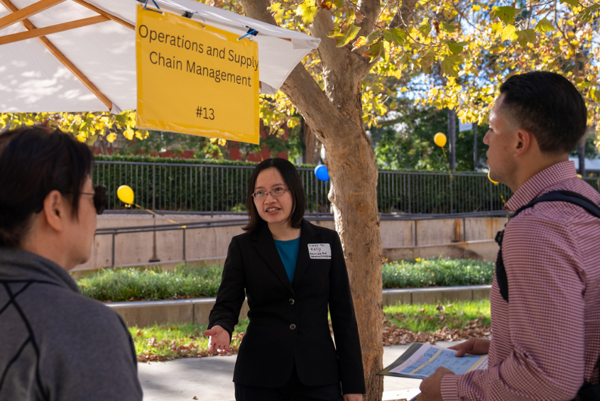 professor talking to students at a business fair