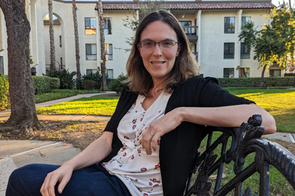 Staff member seated on bench on campus smiling