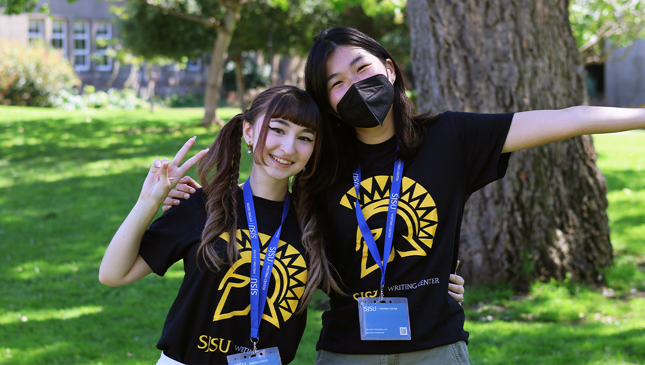 Two Writing Center team members posing on campus lawn and wearing team t-shirts